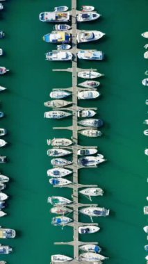 Dikey ekran: Limanın turkuaz suyla hava görüntüsü, deniz kenarında sakin bir atmosfer oluşturan düzenli tekne sıralarını gösteriyor. Dikey perspektif memnun edici deseni vurgular