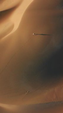 Dikey Ekran: Genç bir kadın büyüleyici bir ışığın altında, sakin ve huzurlu bir ortamda, yalnızlığın ve doğanın güzelliğini yansıtan engin bir çölde yürüyor.