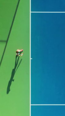 Dikey Ekran: Bir tenisçi mavi kortta oynanan heyecan verici bir maçta atletizm gösteriyor, dinamik hareket ve maharetli bir oyun sergiliyor, enerjiyi ve sportmenliği somutlaştırıyor.