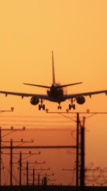 Bir ticari uçak gün batımında, şehir manzarası üzerinde parlayan pist ışıklarıyla zarif bir şekilde iniyor, bir akşam uçuşunun özünü ve alçalan bir uçağı yakalıyor.