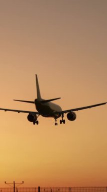 Havacılık, seyahat ve genişleyen gökyüzünün özünü özetleyen canlı bir turuncu gün batımı arkaplanına, alacakaranlıkta yumuşak bir şekilde iniş yapan bir uçak gibi çarpıcı bir sahne gözler önüne seriliyor.