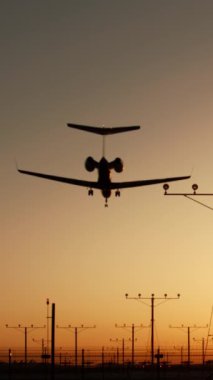 Dikey ekran: Dikey bir video günbatımında podyum ışıklarıyla havacılık fotoğrafçılarına hitap eden bir uçağın iniş yaptığını gösteriyor. Sahne, uçağın yere inişini büyüleyici bir şekilde gösteriyor.