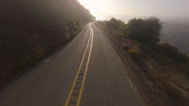 Bir FPV İHA Malibu, California 'daki virajlı bir yolun hava görüntüsünü yakaladı. Bereketli yeşilliklerle çevrili güneş ışığı yolu, dingin ve büyüleyici bir manzara yaratır.