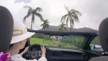 Kaygısız bir kadın üstü açık arabasını Oahus 'un yemyeşil bahçesinde sürüyor. Yüzü, tropikal ada atmosferinin verdiği hazla aydınlanıyor. 4K görüntü. 