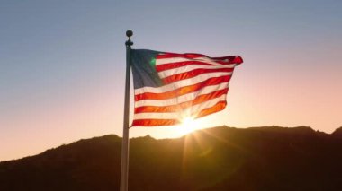 Amerikan bayrağı nefes kesen bir gündoğumu altında sallanıyor, nesillerdir değer verilen vatanseverlik, özgürlük ve bağımsızlık değerlerini sembolize ediyor, ulusların gurur ve mirasını somutlaştırıyor.