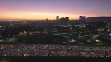 Canlı şehir Los Angeles batan güneşin parlaklığıyla aydınlanıyor ve yoğun bir trafik akışına sahip kalabalık bir şehir manzarası sergiliyor. Şehrin metropolitan atmosferini yakalıyor.