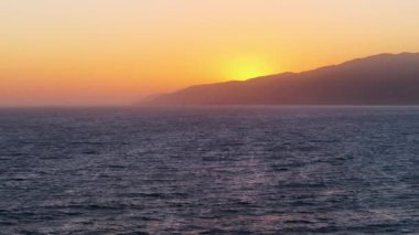 California, ABD 'de huzurlu bir Malibu gün batımının büyüleyici hava görüntüsü. Tepeler, altın suya karşı güneş batarken parlıyor ve okyanus üzerinde muhteşem bir manzara yaratıyor.