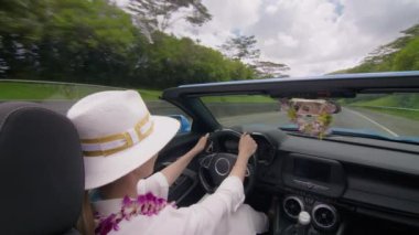 Üstü açık şık bir arabadaki bir kadın güneşli havadan zevk alır, parlak, çekici bir gülümsemeyle Oahus 'un görkemli rotaları boyunca araba sürer. 4K görüntü. 