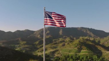 Gün doğumunda veya günbatımında dağların üzerinde dalgalanan Amerikan bayrağı vatanseverliğin, özgürlüğün ve zengin bir mirasın güçlü bir sembolüdür. Ülke için ulusal gurur ve saygıyı temsil eder.