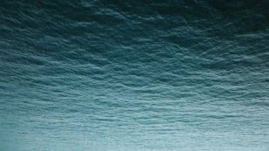 Sakinleştirici dalgalarla okyanusun havadan çekilmiş görüntüsü. Suyun yüzeyi dokulu ve soyut bir kaliteye sahiptir. Görüntü denizin güzelliğini ve dinginliğini minimalist bir şekilde yansıtıyor..
