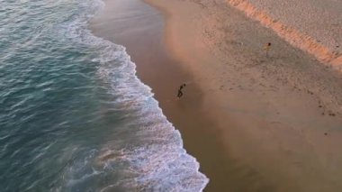 Newport Beach, Kaliforniya, ABD - 17 Aralık 2024: Çarpıcı bir 4K hava çekimi, sakin sahil şeridi, kumlu plajları ve sakin dalgalarıyla güzelliği gösteriyor. Bir insan bu resimde sahil boyunca yürür.