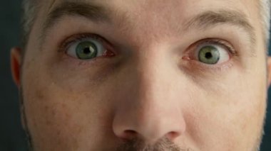 Hoş bir yakın plan çekimde, karizmatik bir adam doğrudan kameraya bakar, komik, renkli yüz hatlarıyla bir dizi ifade eder.