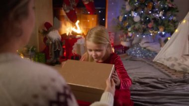 Bir çocuğun güzel dekore edilmiş bir evde annesinin yardımıyla Noel hediyesinin içindeki harikaları keşfettiği büyülü anı izleyin. 4K görüntü. 