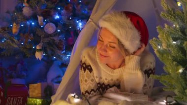 Bu görüntü, Noel 'in tadını çıkaran neşeli bir kadını Noel Baba şapkasıyla süslenmiş ve yanıp sönen ışıklarla çevrili bir şekilde yakalıyor. 4K görüntü. 