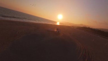 FPV insansız hava aracı Malibu, Kaliforniya 'da nefes kesici ve renkli bir gün batımı yakalıyor. Martılar kıyı şeridi boyunca zarifçe süzülüyorlar.