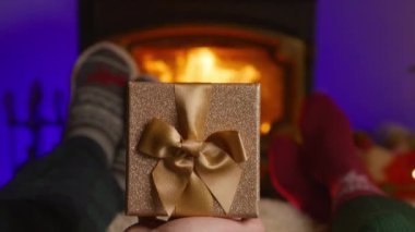 Yürek ısıtan bir sahnede, bir erkek, güzel bir şekilde paketlenmiş bir Noel hediyesini, birlikte şenlik sezonunun neşesini ve sıcaklığını paylaştıkları sıcak şöminenin önünde, karısına sunar.