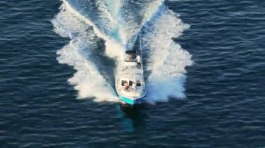 Bir hava manzarası, altındaki göz kamaştırıcı, ışıl ışıl okyanus dalgalarının üzerinde süzülen hızlı bir tekneyi yakalar.