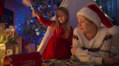 Hassas bir anda yakalanan bir kız, Noel Baba 'ya yazdığı mektubu annesinin gözünün önünde, rahat ve aydınlık bir Noel ortamında sihirli bir posta kutusuna koyar. 4K görüntü. 