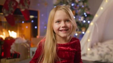 Kırmızı şenlikli bir elbise giymiş genç bir kız Noel dekoruyla çevrili bir şekilde şakacı bir şekilde dilini uzatır ve saf bir eğlence anını yakalar. 4K görüntü. 