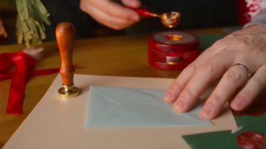 Yakından bakınca, bir adamın güzel tasarlanmış bir Noel zarfına ustalıkla sıvı pul yapıştırarak neşeli tatil sezonunun yaratıcılığını ve sanatsal ifadesini vurguladığını görüyoruz.