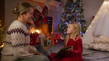 Neşeli bir Noel sahnesinde bir anne, mutlu kızına güzel bir hediye sunar. Bir şenlik ağacı tarafından. 4K görüntü. 
