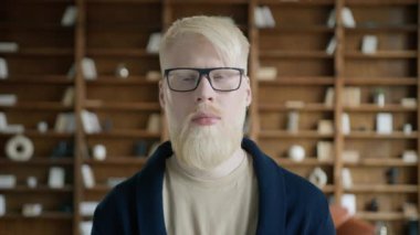 Ciddi albino işadamı kameraya kapalı gözlerle poz veriyor. Arka planda kitap raflarıyla kütüphanede duran kendine güvenen bir adamın portresi. Gözlük takan düşünceli adam yüzü, yavaş çekim.