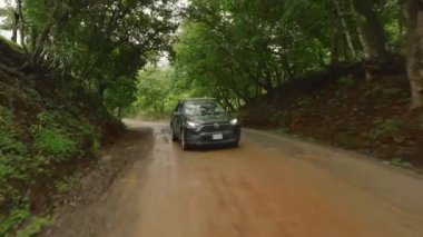 Kosta Rika, Juli 2024: Güzel Kosta Rika 'nın canlı ve gür yeşillikleri arasında zorlu ve zorlu bir orman yolunda ustaca yol alan bir araba, nefes kesici 4K hava görüntülerinde yer aldı