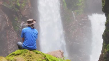 Genç bir çocuk Kosta Rika 'daki şelalenin tadını çıkarıyor. Yeşilliklerle çevrili, 4K' daki doğal güzelliğin özünü yakalıyor.