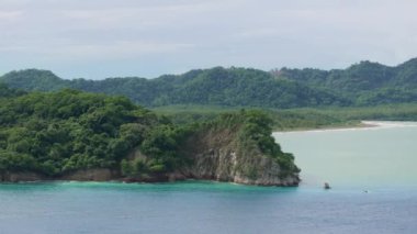 Bu nefes kesici hava fotoğrafı Puntarenas, Kosta Rika 'nın büyüleyici güzelliğini yakalıyor, yemyeşil tepeleri ve yumuşak, bulutlu bir gökyüzünün altındaki sakin turkuaz suları vurguluyor.
