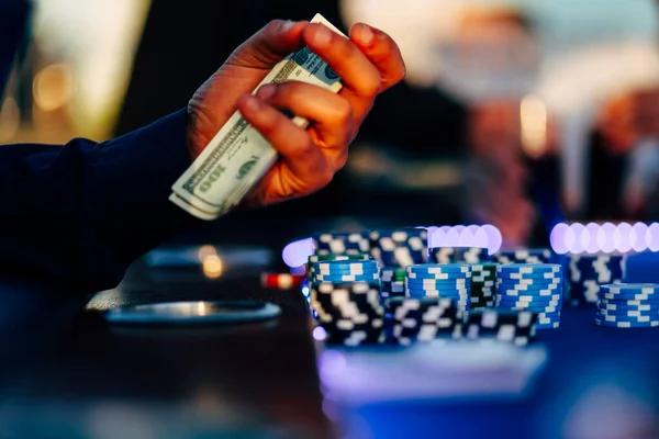 男赌徒手里拿着现金坐在轮盘赌旁边 桌上放着赌场的筹码 — 图库照片