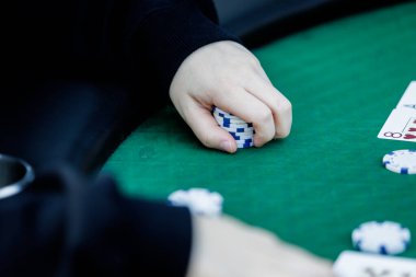 Poker fişlerini karıştırırken ve yüksek bahisli bir oyunda kart tutarken çekilmiş detaylı bir çekim. Çiplerin canlı renkleri ve kartların canlı dokuları anın enerjisini ve gerilimini vurguluyor.