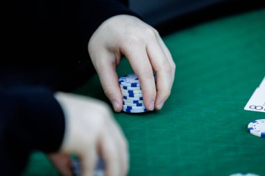 Poker fişlerini karıştırırken ve yüksek bahisli bir oyunda kart tutarken çekilmiş detaylı bir çekim. Çiplerin canlı renkleri ve kartların canlı dokuları anın enerjisini ve gerilimini vurguluyor.