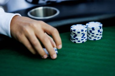 Poker fişlerini karıştırırken ve yüksek bahisli bir oyunda kart tutarken çekilmiş detaylı bir çekim. Çiplerin canlı renkleri ve kartların canlı dokuları anın enerjisini ve gerilimini vurguluyor.