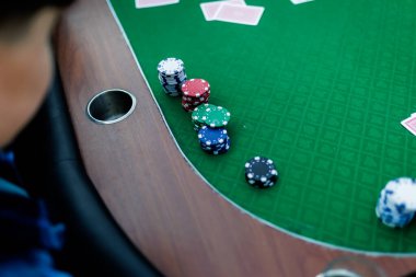 Poker fişlerini karıştırırken ve yüksek bahisli bir oyunda kart tutarken çekilmiş detaylı bir çekim. Çiplerin canlı renkleri ve kartların canlı dokuları anın enerjisini ve gerilimini vurguluyor.