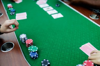 Poker fişlerini karıştırırken ve yüksek bahisli bir oyunda kart tutarken çekilmiş detaylı bir çekim. Çiplerin canlı renkleri ve kartların canlı dokuları anın enerjisini ve gerilimini vurguluyor.