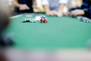 Poker fişlerini karıştırırken ve yüksek bahisli bir oyunda kart tutarken çekilmiş detaylı bir çekim. Çiplerin canlı renkleri ve kartların canlı dokuları anın enerjisini ve gerilimini vurguluyor.