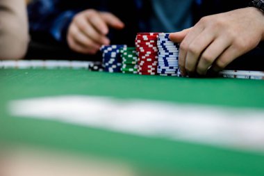 Poker fişlerini karıştırırken ve yüksek bahisli bir oyunda kart tutarken çekilmiş detaylı bir çekim. Çiplerin canlı renkleri ve kartların canlı dokuları anın enerjisini ve gerilimini vurguluyor.