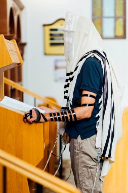 Yahudi adam, Bar Mitzvah kutlamasından önce İsrail sinagogunda Tevrat 'ı okumak için dua ediyor. Sağ tarafta Tefillin var..
