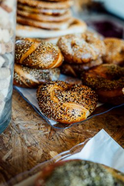 Geleneksel hasır sepete dizilmiş taze pişmiş susamlı simit. Altın kahverengi kabuk cömertçe susam tohumları serpiştiriliyor ve çıtır çıtır bir doku oluşturuyor. Arka plan hafifçe bulanık, kırsal ve sanatsal bir his ekliyor.