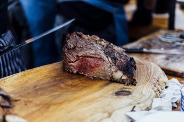 Bir barbekü etkinliği sırasında tahta kesme tahtasıyla taze dilimlenen sulu füme et eti. Yakın plan taze et, kavrulmuş bir kabuk, doğal ışık altında yakalanır. 