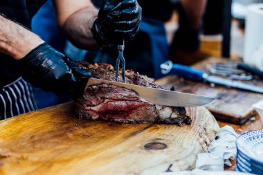 Bir barbekü etkinliği sırasında tahta kesme tahtasıyla taze dilimlenen sulu füme et eti. Yakın plan taze et, kavrulmuş bir kabuk, doğal ışık altında yakalanır. 