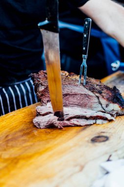 Bir barbekü etkinliği sırasında tahta kesme tahtasıyla taze dilimlenen sulu füme et eti. Yakın plan taze et, kavrulmuş bir kabuk, doğal ışık altında yakalanır. 