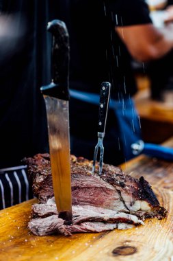 Bir barbekü etkinliği sırasında tahta kesme tahtasıyla taze dilimlenen sulu füme et eti. Yakın plan taze et, kavrulmuş bir kabuk, doğal ışık altında yakalanır. 