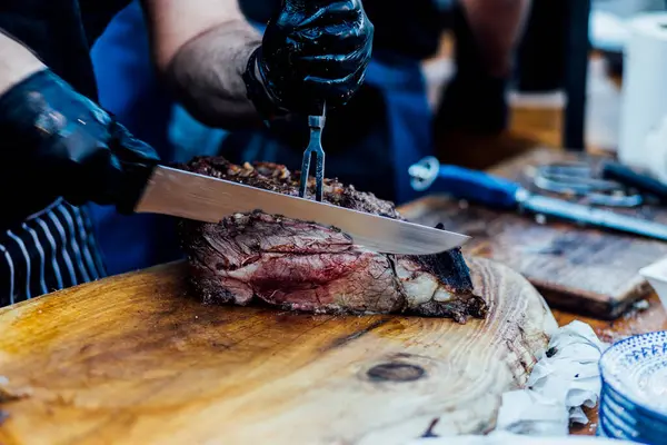 Bir barbekü etkinliği sırasında tahta kesme tahtasıyla taze dilimlenen sulu füme et eti. Yakın plan taze et, kavrulmuş bir kabuk, doğal ışık altında yakalanır. 