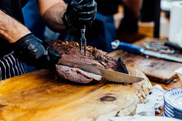 Bir barbekü etkinliği sırasında tahta kesme tahtasıyla taze dilimlenen sulu füme et eti. Yakın plan taze et, kavrulmuş bir kabuk, doğal ışık altında yakalanır. 