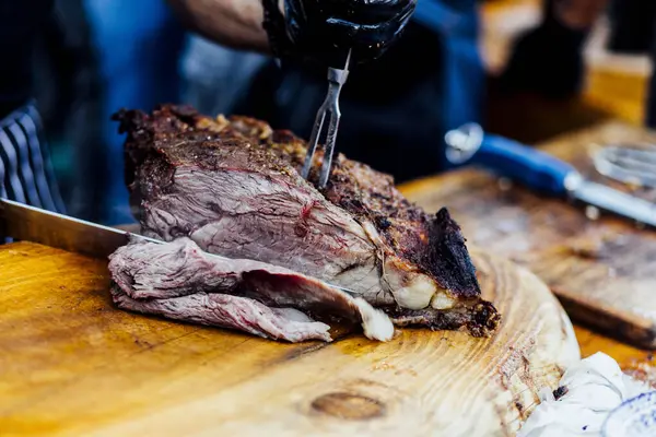Bir barbekü etkinliği sırasında tahta kesme tahtasıyla taze dilimlenen sulu füme et eti. Yakın plan taze et, kavrulmuş bir kabuk, doğal ışık altında yakalanır. 