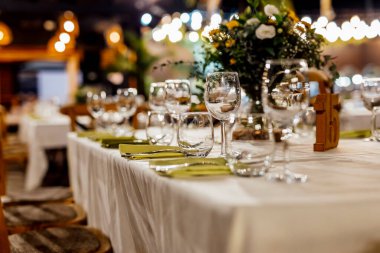 Şarap kadehleri ve çiçekli yemek masası, düğün için mükemmel, zarif bir parti ya da açık hava kutlaması için. Sıcak ışıklar ve yumuşak bokeh samimi ve lüks bir atmosfer yaratır..