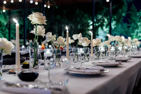 Şarap kadehleri ve çiçekli yemek masası, düğün için mükemmel, zarif bir parti ya da açık hava kutlaması için. Sıcak ışıklar ve yumuşak bokeh samimi ve lüks bir atmosfer yaratır..