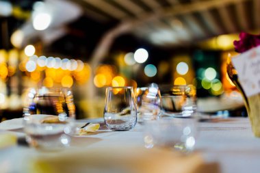 Şarap kadehleri ve çiçekli yemek masası, düğün için mükemmel, zarif bir parti ya da açık hava kutlaması için. Sıcak ışıklar ve yumuşak bokeh samimi ve lüks bir atmosfer yaratır..