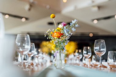 Şarap kadehleri ve çiçekli yemek masası, düğün için mükemmel, zarif bir parti ya da açık hava kutlaması için. Sıcak ışıklar ve yumuşak bokeh samimi ve lüks bir atmosfer yaratır..